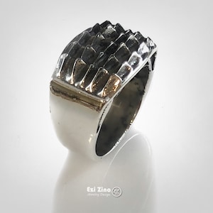 May include: A silver ring with a textured, geometric design on the top. The ring is made of metal and has a polished finish.