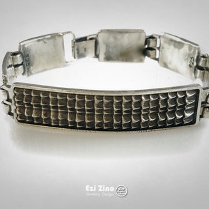 May include: A silver bracelet with a textured, rectangular center piece. The bracelet is made of linked silver pieces and has the number "925" stamped on the back.