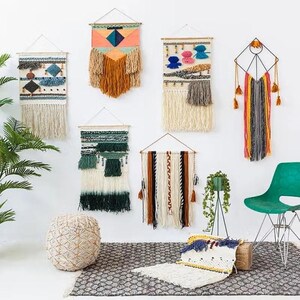 K&ouml;nnte beinhalten: Eine Sammlung handgefertigter Wandbeh&auml;nge in verschiedenen Gr&ouml;&szlig;en und Designs. Die Textilkunstwerke weisen eine Mischung aus Farben, Texturen und Mustern auf, darunter Fransen, geometrische Formen und gewebte Details. Die Dekoration wird an einer wei&szlig;en Wand pr&auml;sentiert.