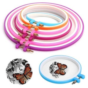 May include: A set of five nested circular embroidery hoops in varying sizes and colors, including purple, pink, orange, and light blue. Each hoop features a metal tension screw mechanism. A light blue hoop holds a white fabric with a butterfly design.