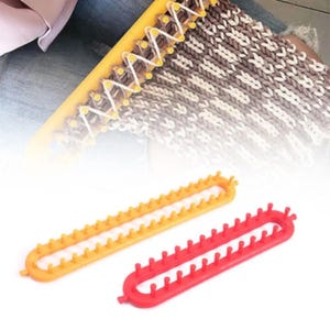 May include: Two plastic knitting looms, one orange and one red, are displayed against a white background. The looms are rectangular with pegs along the inner edges. A yellow loom with a knitted project is also visible.