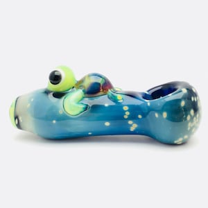 May include: A blue glass pipe with a small green turtle figurine on top. The pipe has a white speckled design and a blue bowl.