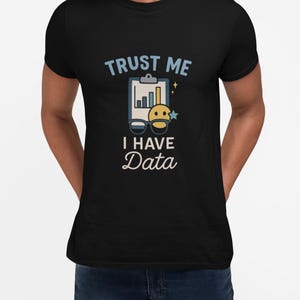 May include: Black t-shirt featuring the text "TRUST ME I HAVE Data" in light blue. The design includes a chart, glasses, and a smiling face with a star. This is a casual wear item.