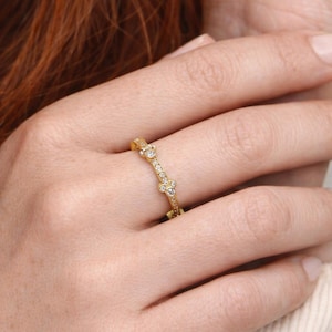 May include: A delicate gold ring featuring a series of small, sparkling gemstones. The ring has a repeating pattern of gemstones and is worn on a finger. The ring is a piece of jewelry.