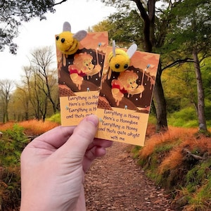 May include: Two handmade yellow and gray bee-shaped ornaments are attached to cards with a Winnie the Pooh theme. The cards have text that reads "Everything is Honey, Here's a Honeybee, Everything is Honey and that's quite alright with me."