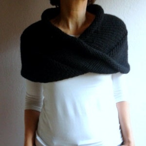 May include: A black knitted cowl neck scarf with a wide, folded collar. The scarf is worn over a white long-sleeved shirt and blue jeans.