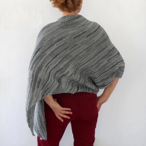 Pu&ograve; includere: Scialle di maglia a righe grigio e nero con una vestibilit&agrave; ampia e drappeggiata. Lo scialle &egrave; indossato da una persona con pantaloni rossi.