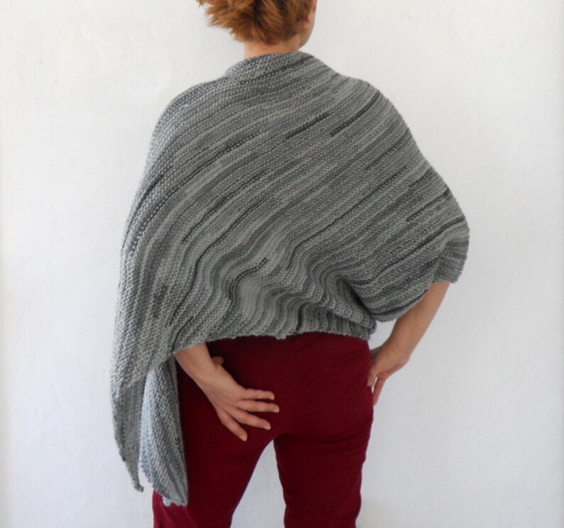 Pu&ograve; includere: Scialle di maglia a righe grigio e nero con una vestibilit&agrave; ampia e drappeggiata. Lo scialle &egrave; indossato da una persona con pantaloni rossi.