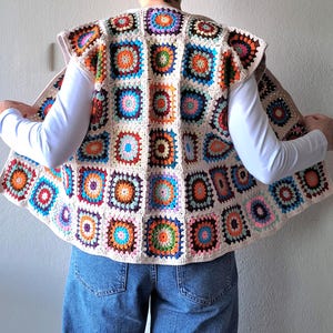 May include: A crocheted vest with a colorful geometric pattern. The vest is sleeveless and has a rounded hem. It is made of a cream-colored yarn and features a variety of colors, including red, orange, yellow, green, blue, and purple.