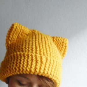 May include: A yellow knitted beanie with cat ears. The beanie is made of a soft, warm yarn and is perfect for keeping your head and ears warm in the winter.