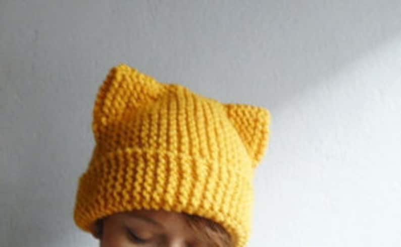 May include: A yellow knitted beanie with cat ears. The beanie is made of a soft, warm yarn and is perfect for keeping your head and ears warm in the winter.