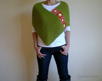 Op de afbeelding: Een groene gebreide poncho met een rode en witte gehaakte rand. De poncho wordt gedragen over een wit shirt en een blauwe jeans.
