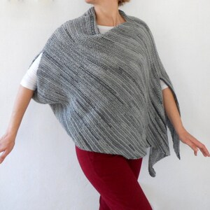 Pu&ograve; includere: Un poncho di maglia a righe grigio e nero con scollo drappeggiato. Il poncho &egrave; indossato sopra una maglietta bianca e pantaloni rossi.