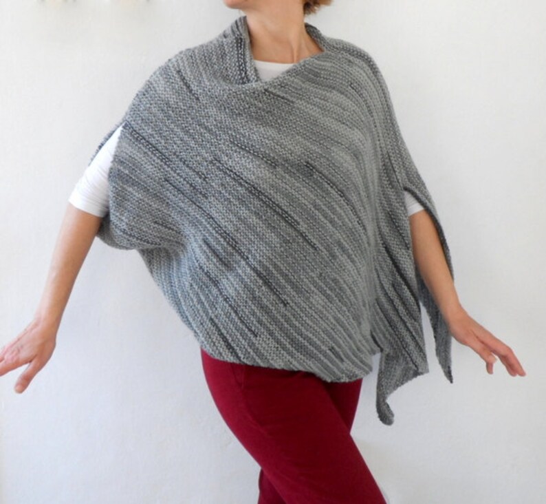Pu&ograve; includere: Un poncho di maglia a righe grigio e nero con scollo drappeggiato. Il poncho &egrave; indossato sopra una maglietta bianca e pantaloni rossi.