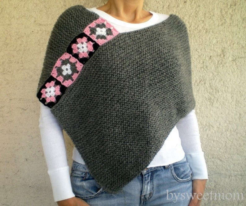 Puede incluir: Poncho de punto gris con ribete de ganchillo rosa y blanco. El ribete presenta una serie de dise&ntilde;os cuadrados con flores.