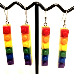 May include: Four pairs of colorful earrings, each featuring a vertical stack of toy building blocks in a rainbow color scheme. The blocks are red, orange, yellow, green, blue, and purple. The earrings hang from silver-colored hooks.