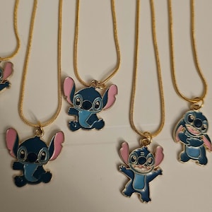 Puede incluir: Varias cadenas doradas con colgantes con el personaje de dibujos animados Stitch. Los colgantes son azules con orejas y detalles rosas. Las cadenas se muestran sobre un fondo blanco.