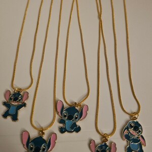 Puede incluir: Varias cadenas doradas, cada una con un colgante que representa un personaje de dibujos animados azul con orejas rosas. Los colgantes est&aacute;n en varias poses, con un cierre dorado.