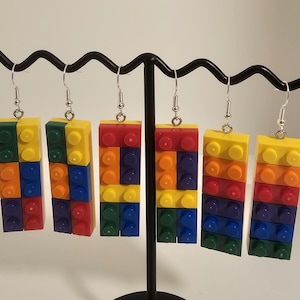 May include: Six colorful brick-style earrings in red, yellow, blue, green, and orange hang from a black display stand. Each earring is made of stacked blocks with silver-tone ear wires. The earrings are a fun, playful accessory.