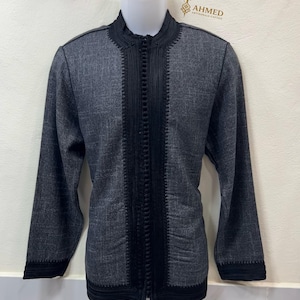 May include: A gray caftan with black trim and a mandarin collar. The caftan has a full-length zipper and is displayed on a mannequin. The caftan has the text "AHMED ARTISANALS CAFTAN" in gold lettering.