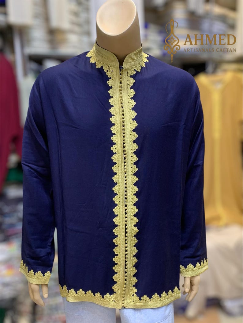 May include: A navy blue caftan with gold trim and detailing. The caftan features gold embroidery along the collar, front opening, and cuffs. The caftan is displayed on a mannequin. The text "AHMED ARTISANALS CAFTAN" is visible.