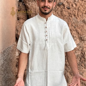 May include: A short-sleeved, off-white shirt featuring a mandarin collar and a front placket with five brown buttons. The shirt has a textured appearance and is worn with dark gray shorts. The text AHMED is visible in the upper left corner.