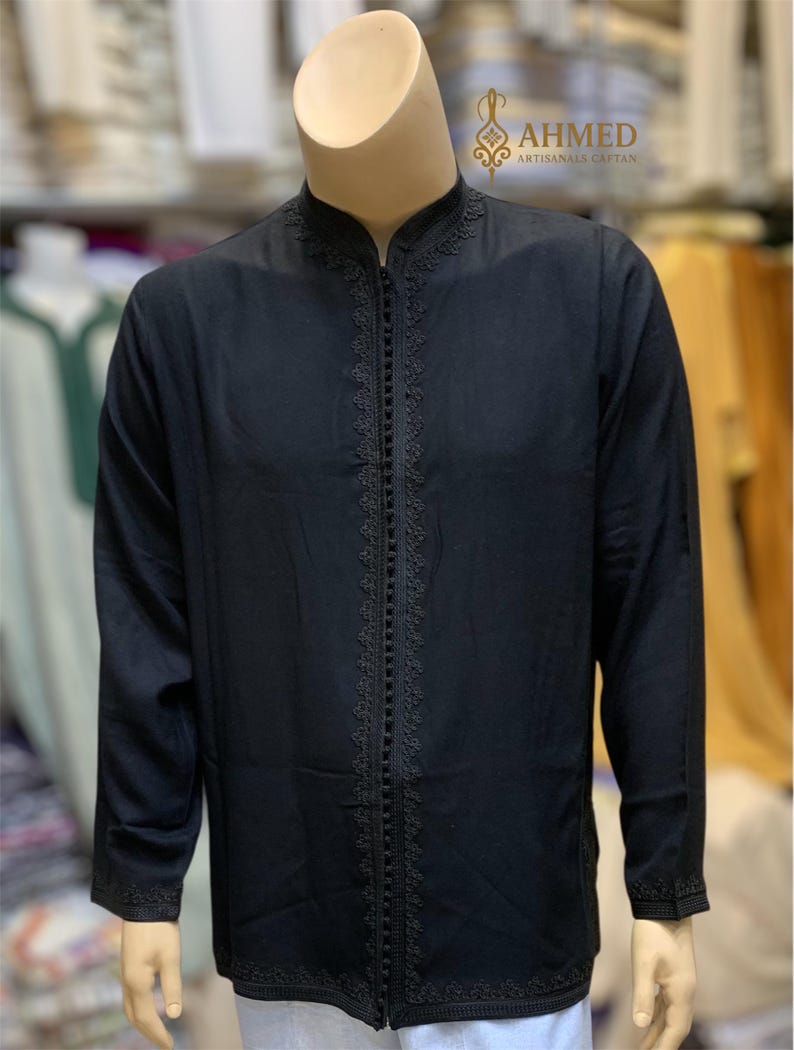 May include: Black caftan with intricate embroidery along the zipper and cuffs, displayed on a mannequin. The caftan has a mandarin collar and long sleeves. The text "AHMED ARTISANALS CAFTAN" is visible in the upper right corner.