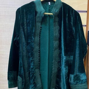 May include: A dark green velvet jacket with a mandarin collar and long sleeves. The jacket has decorative trim and a buttoned front. The brand name "AHMED" is visible on the hanger. The jacket is a rich, deep green.