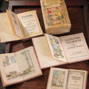 May include: A selection of vintage miniature books, including titles such as "Pierre" and "Alligators All Around" by Maurice Sendak. The books feature colourful illustrations and are displayed on a dark wooden surface. The books are from the Nutshell Library.