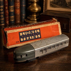 May include: A vintage Lionel Electric Trains model passenger car with a dark gray rounded nose and a silver corrugated metal body. The car is positioned in front of its original orange cardboard box, which features the Lionel Electric Trains logo.