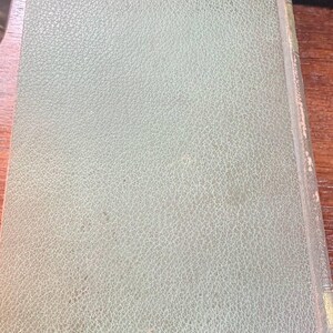 May include: A vintage book with a textured, pale green cover. The cover has a subtle, mottled pattern and a slightly worn appearance. The book's spine is visible, showing the binding and edges.
