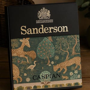 May include: A decorative box with a black top and a patterned front featuring deer, leopards, and trees in shades of green, brown, and beige. The word "Sanderson" is in gold lettering, and the word "CASPIAN" is also visible.