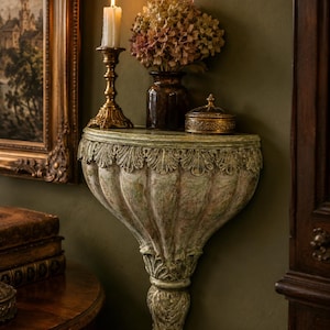 May include: A wall-mounted semi-circular console shelf featuring a distressed pale green and white finish with carved acanthus leaf detailing along the top edge and a tapered, fluted base that extends downward to a decorative point.