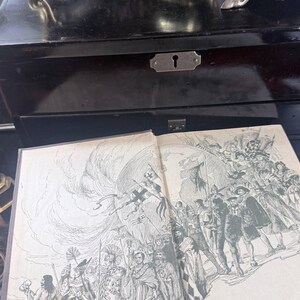 May include: An open book featuring a detailed black and white illustration of a historical scene. The book rests on a dark wooden surface, with a black box and decorative items in the background. The illustration depicts a procession.