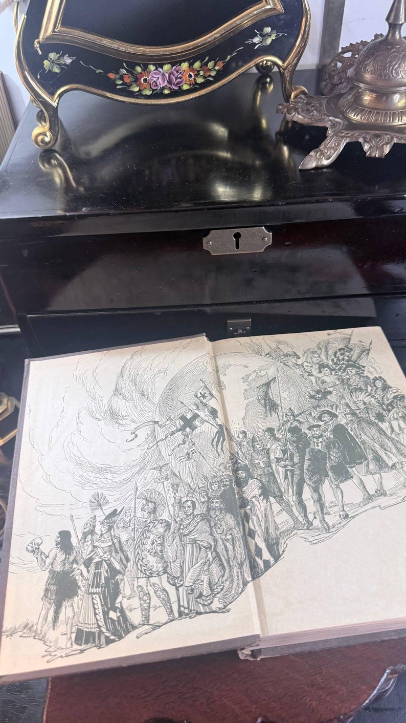 May include: An open book featuring a detailed black and white illustration of a historical scene. The book rests on a dark wooden surface, with a black box and decorative items in the background. The illustration depicts a procession.