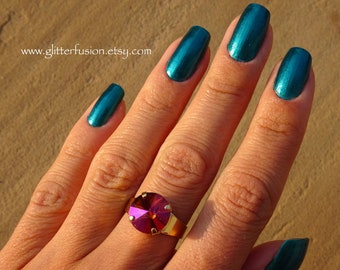 May include: A hand with teal blue nail polish and a ring with a large, pink, faceted gemstone. The ring is on the middle finger of the hand. The background is a light brown color.