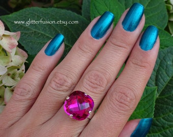May include: A silver ring featuring a large, square-cut, hot pink gemstone. The ring is set against a backdrop of green leaves and a hand with teal nail polish. The website address www.glitterfusion.etsy.com is visible.