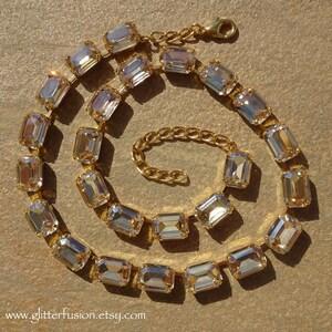 May include: A gold chain necklace with a row of clear, rectangular, faceted crystals. The necklace has a lobster clasp closure.