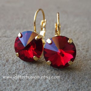May include: A pair of gold-colored leverback earrings with large, faceted, round, ruby-red crystals. The crystals are set in gold-colored prongs. The website address www.glitterfusion.etsy.com is visible at the bottom of the image.