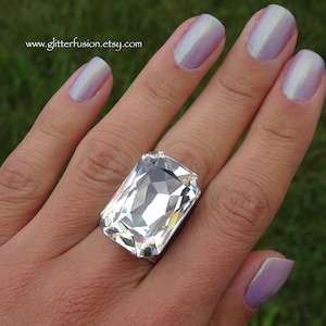 May include: A large, rectangular, clear crystal ring with a silver band. The ring is set on a hand with light purple nail polish. The website address www.glitterfusion.etsy.com is visible in the image.