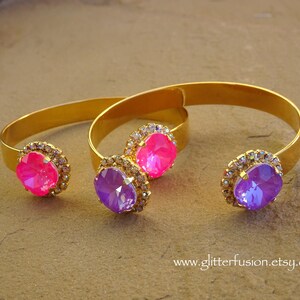 May include: Two gold bangle bracelets with jeweled accents. The bracelets feature a large pink rhinestone and a large purple rhinestone.