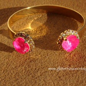 May include: A gold bangle bracelet with two large pink rhinestones set in a clear crystal halo.