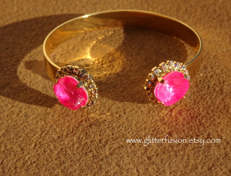May include: A gold bangle bracelet with two large pink rhinestones set in a clear crystal halo.