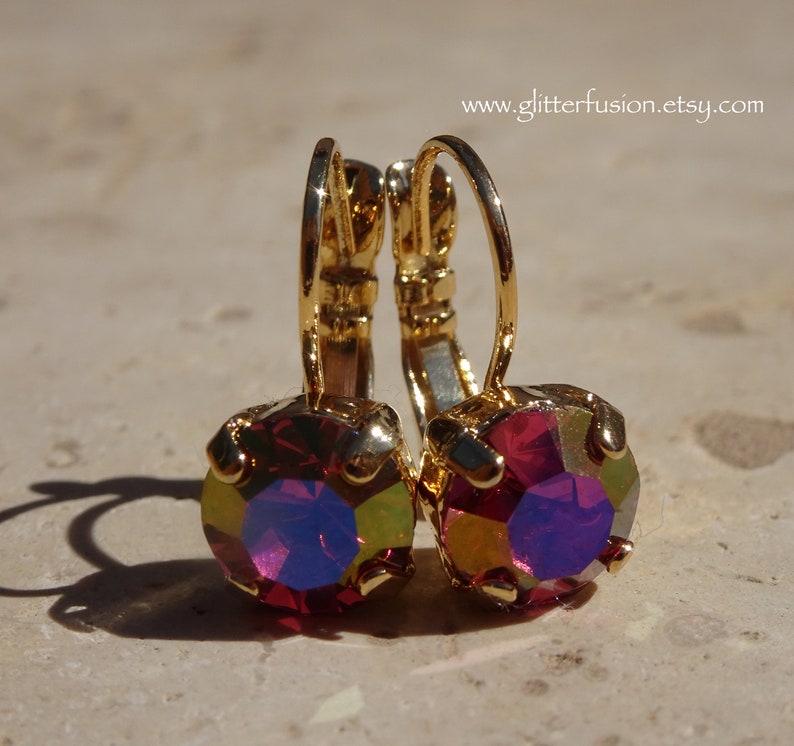 May include: A pair of gold hoop earrings with a red iridescent gemstone in the center of each hoop.