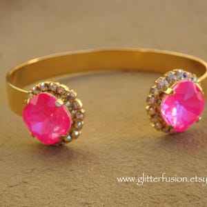 May include: A gold bangle bracelet with two large pink rhinestones set in a halo of smaller clear rhinestones.