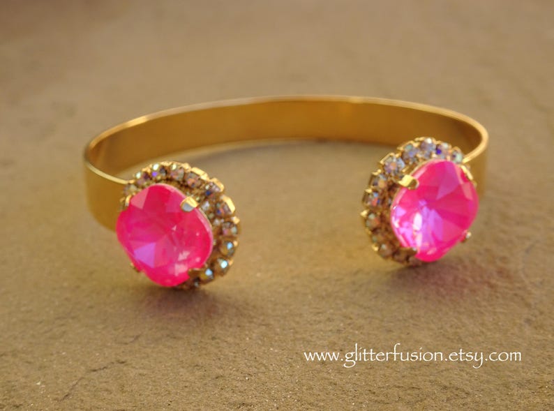 May include: A gold bangle bracelet with two large pink rhinestones set in a halo of smaller clear rhinestones.