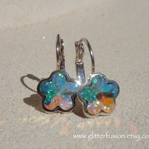May include: A pair of flower-shaped earrings with iridescent, multi-colored crystals set in silver-toned metal. The earrings have a lever-back closure. The website address www.glitterfusion.etsy.com is visible at the bottom of the image.