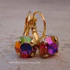 May include: A pair of gold earrings with iridescent pink and green gemstones. The earrings have a lever back closure.