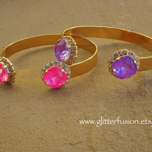 May include: Three gold bangle bracelets with jeweled accents. The bracelets feature a pink, purple, and a light purple rhinestone.