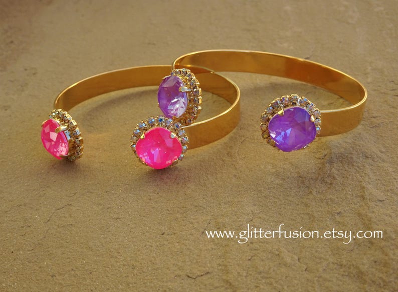 May include: Three gold bangle bracelets with jeweled accents. The bracelets feature a pink, purple, and a light purple rhinestone.